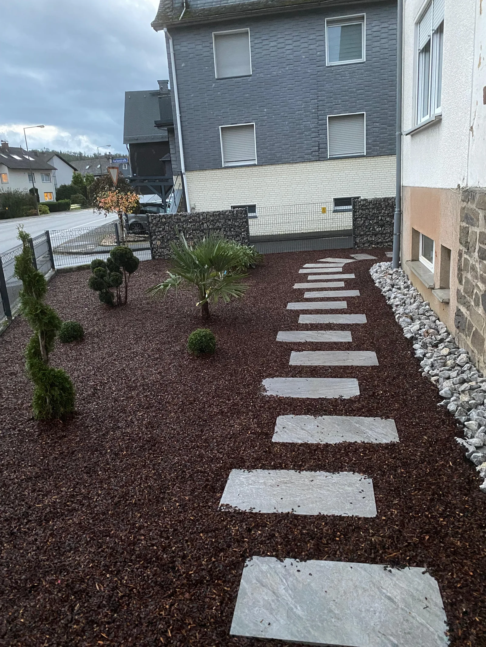Helle Trittplatten führen durch ein bepflanztes Vorgartenbeet mit dunkler Abdeckung